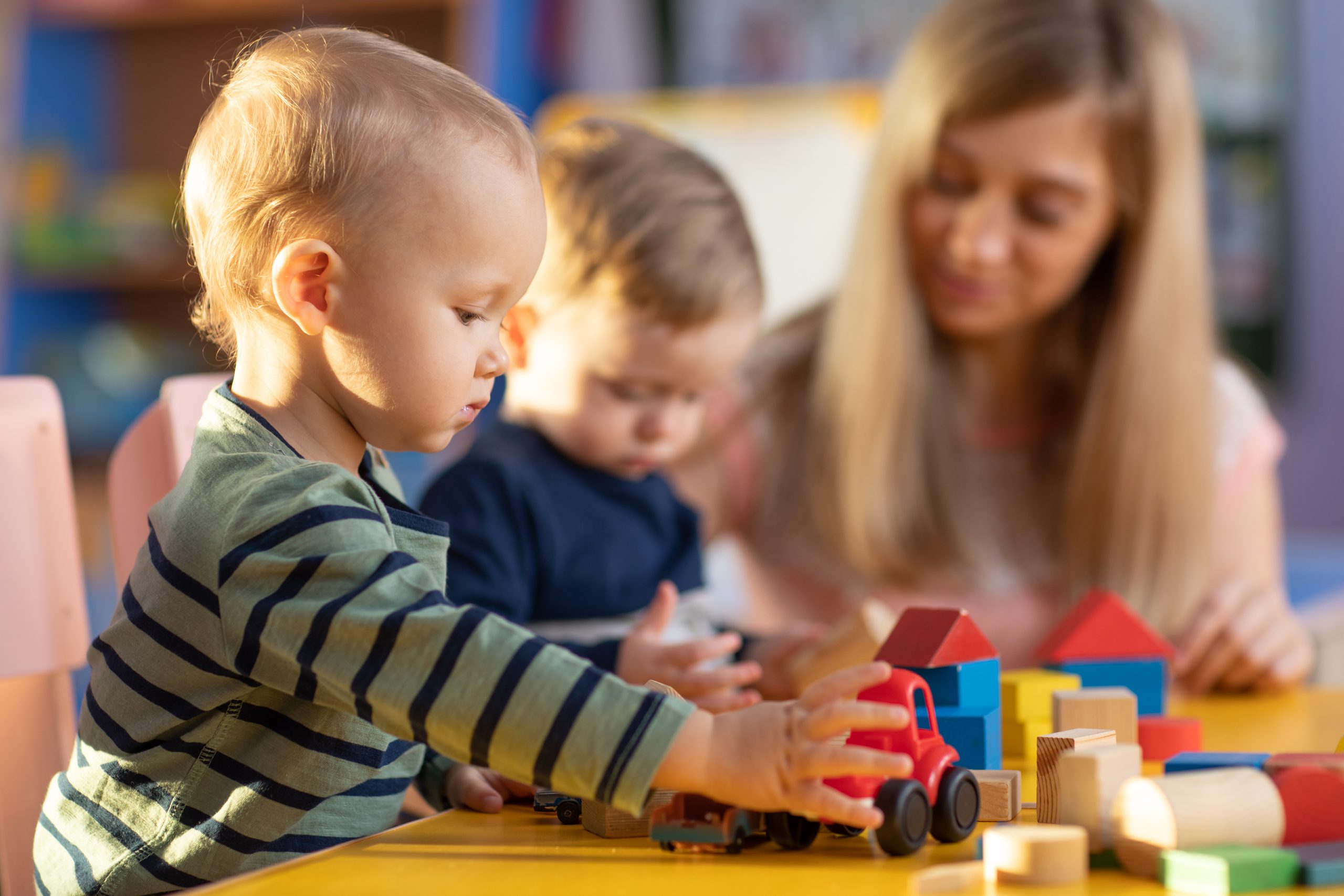 Preschool teacher and cute kids boys playing in kindergarten