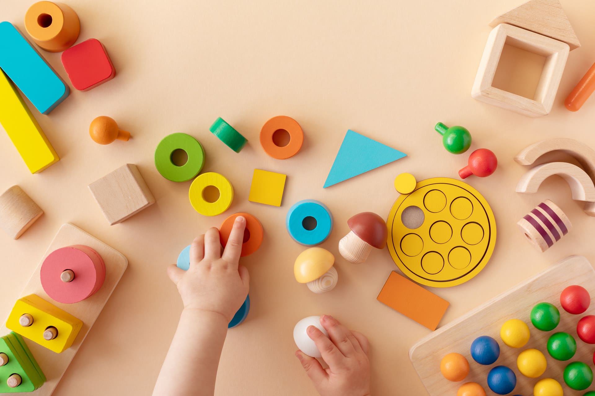 Toddler activity for motor and sensory development. Baby hands with colorful wooden toys on table from above.